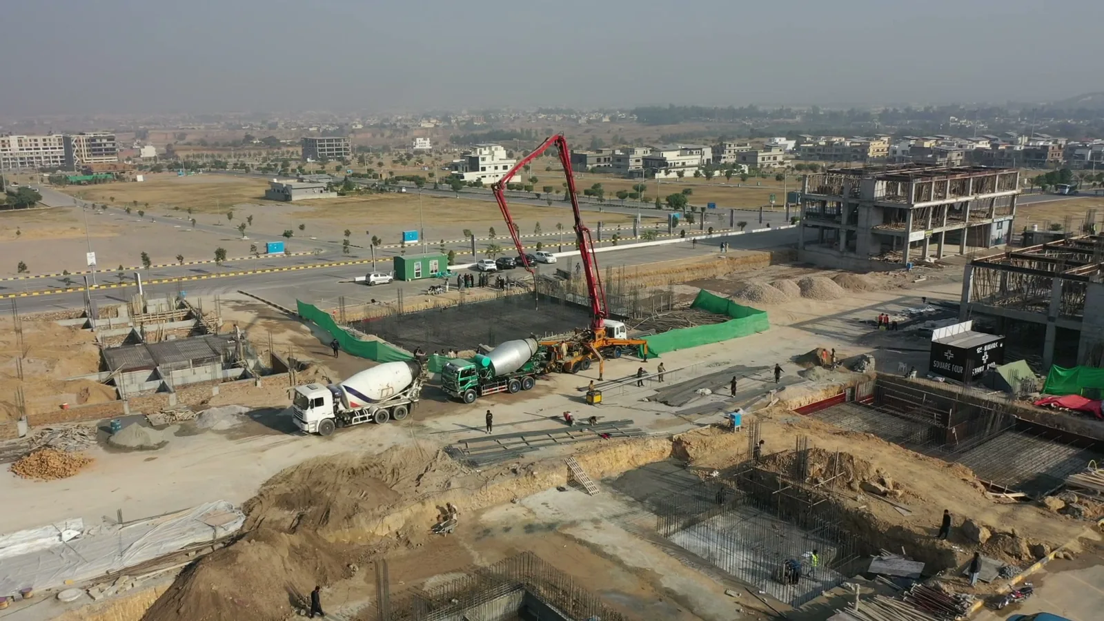 A drone view of a basement slab being poured, with steel reinforcement and footings visible in the open excavation